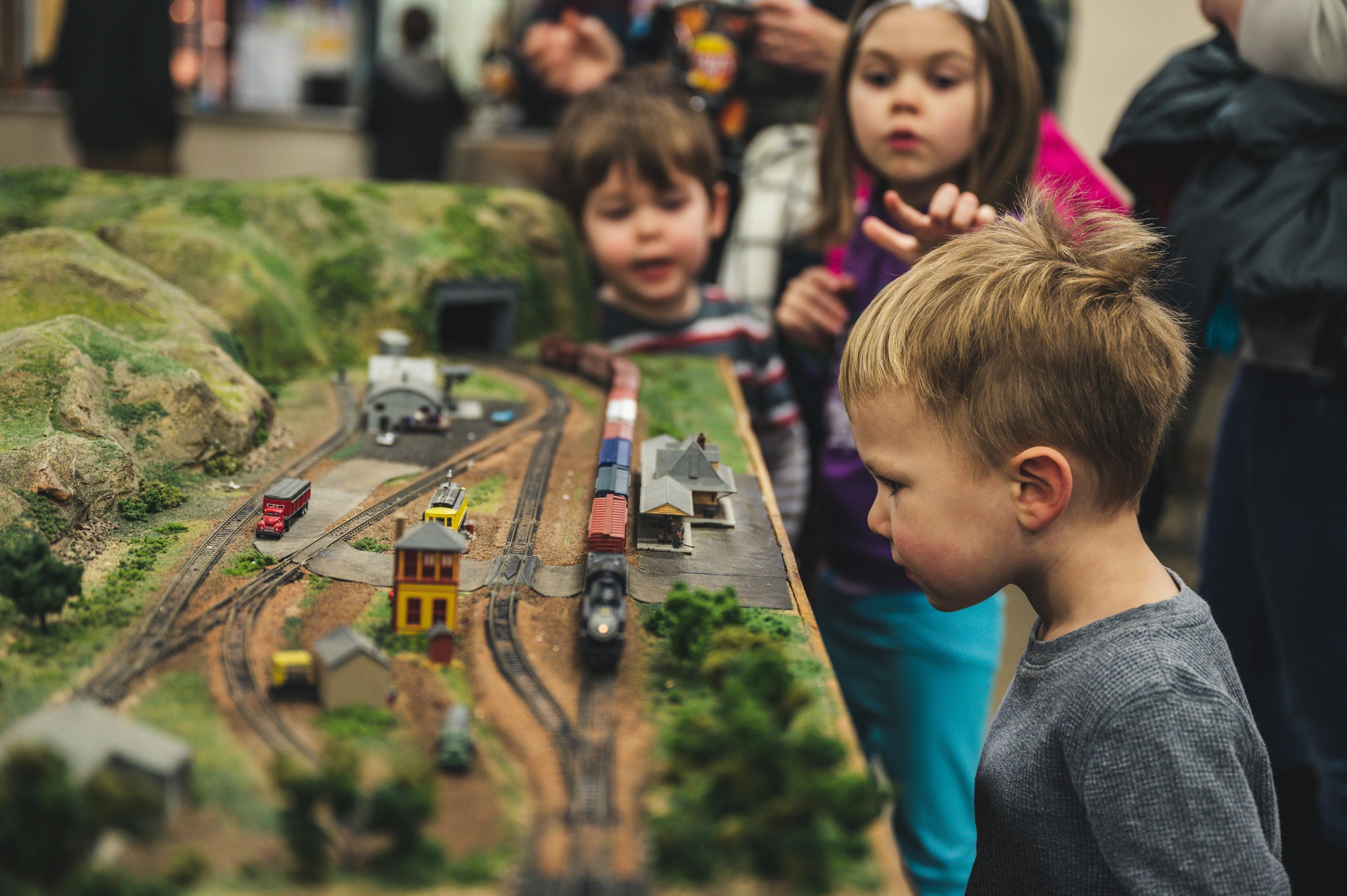 Selektives Fokusfoto Des Jungen, Der Nahe Miniatur Zugspielzeug Steht